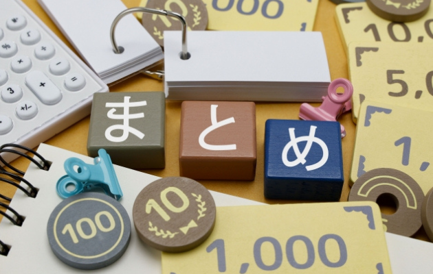 現金のおもちゃ、電卓、ノートに囲まれた中にブロックで「まとめ」と書いてある写真