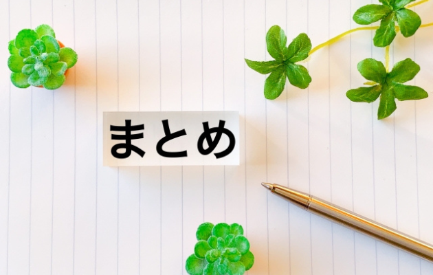ノートの上にまとめとかいてあり、周りにグリーン植物とボールペンが置いてある写真