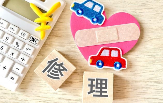 電卓と車と車の間にハートと絆創膏が置いてある写真。周りに積み木で「修理」と書いて修理代を表している写真