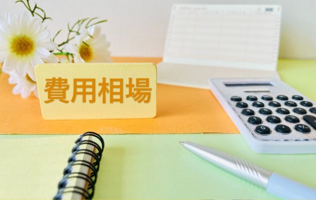 費用相場と書いてある周りに電卓、ボールペン、通帳、ノートが置いてある写真