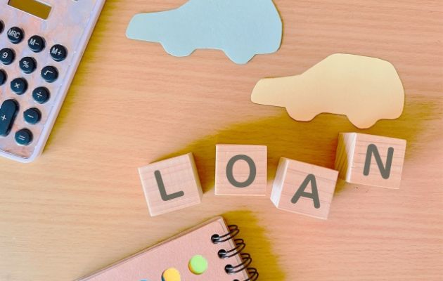 電卓と車の形にくり抜かれた紙が置いてあり、積み木に「LOAN」と書かれている写真
