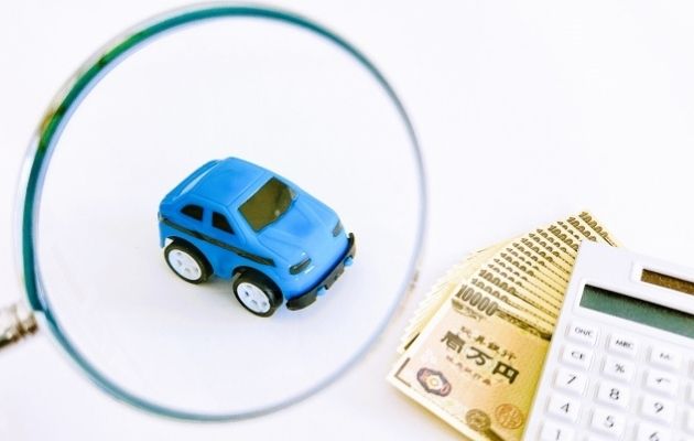 青のおもちゃの車を虫眼鏡で映しており、その横に電卓と1万円が並んでいる写真