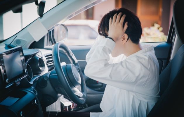 女性が車の中で頭を両手で抱えて、事故してしまった様子の写真