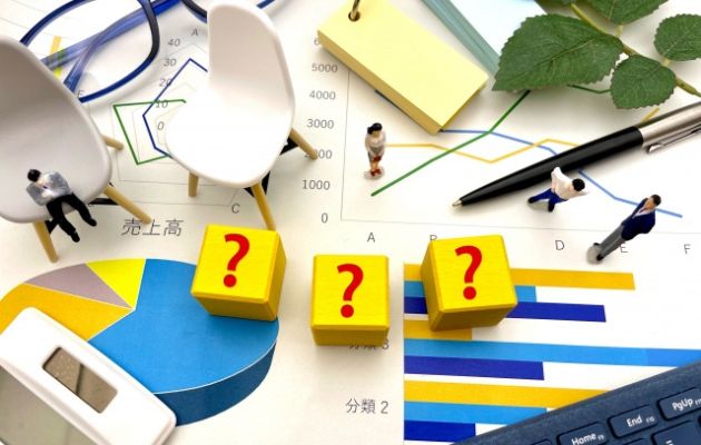 資料の上に黄色のブロックにクエッションマークが書かれたものが3つ並んでいる。周りには人形がおいてあり、下がる理由を考えている様子の写真