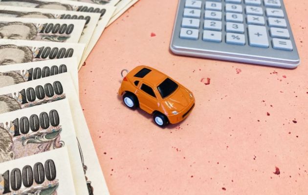 一万円が並んでおり、その横に車のおもちゃと電卓が置いてある写真