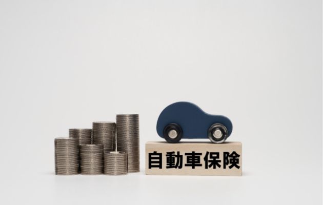 積み木に自動車保険と書かれており、その上におもちゃの自動車が乗っている。積み木の横には硬貨が積み上げられている写真