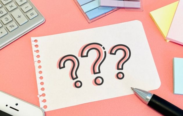 電卓や付箋、携帯が置いてあるところに紙切れで「？？？」とクエッションマークが書かれている写真