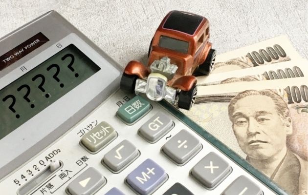 電卓に「？」マークが並んでおり、そこに車のおもちゃと現金1万円が置いてある写真