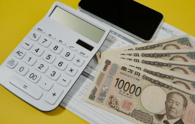 請求書の上に電卓や携帯、10000円の現金が置いてある写真