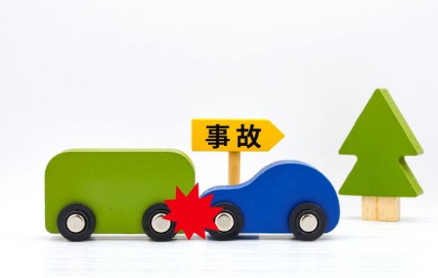 木のおもちゃの車が衝突している様子。その後ろに木札で「事故」と書かれている写真